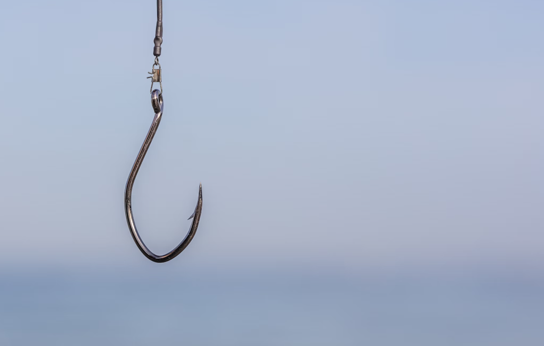 A close-up of a fishing hook suspended against a blurred blue sky background.