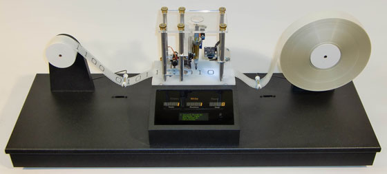 A physical Turing machine model featuring a moving tape with binary digits, a reading/writing head, and a digital display, demonstrating computational principles.